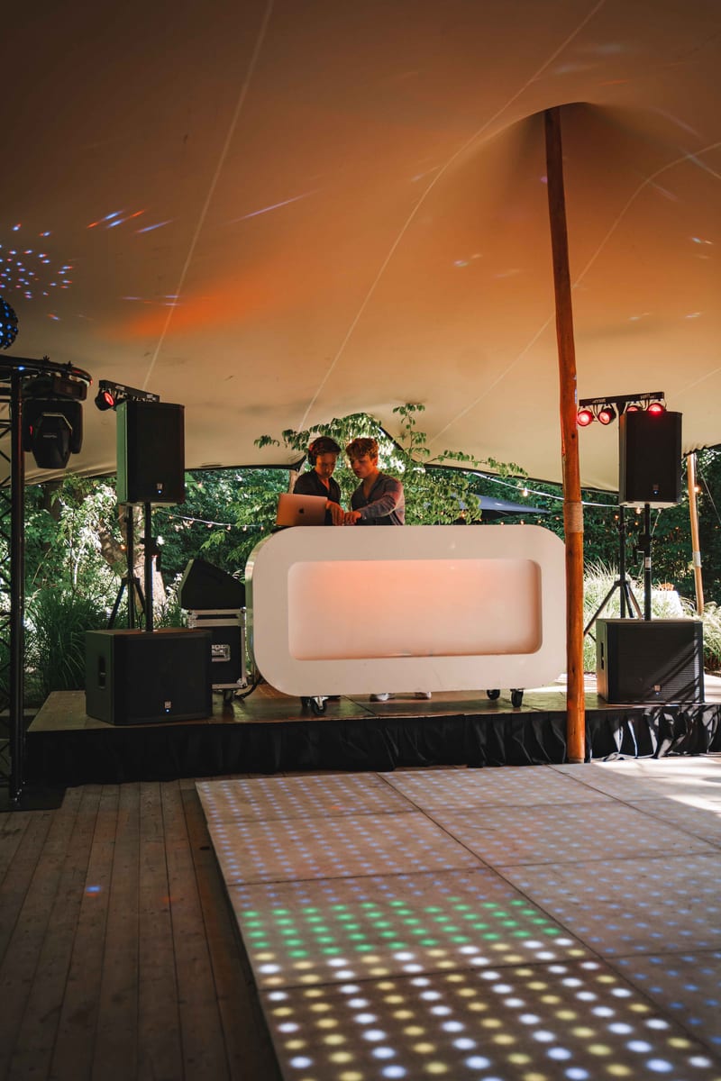 Witte DJ-booth naast een LED-dansvloer in een feesttent