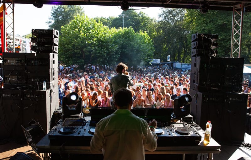 Zicht vanaf de DJ-booth op line-arrays, moving heads en het publiek