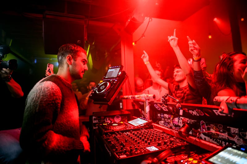 DJ achter CDJ-spelers in rood licht met dansend publiek